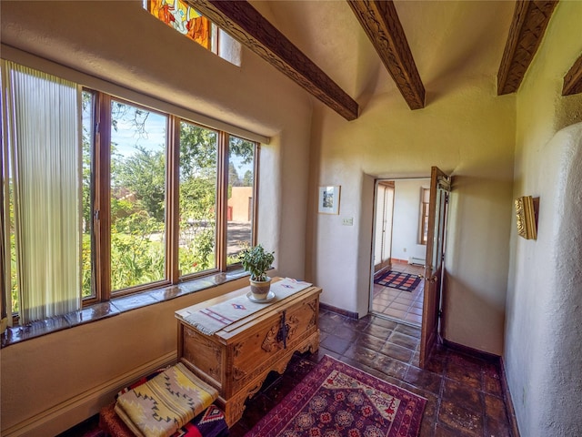 interior space with baseboard heating, stone finish flooring, baseboards, and beamed ceiling