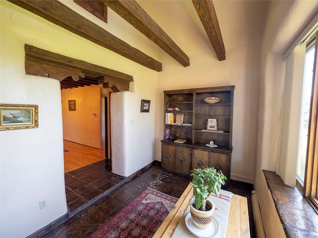 interior space featuring beamed ceiling, baseboards, stone tile flooring, and a healthy amount of sunlight