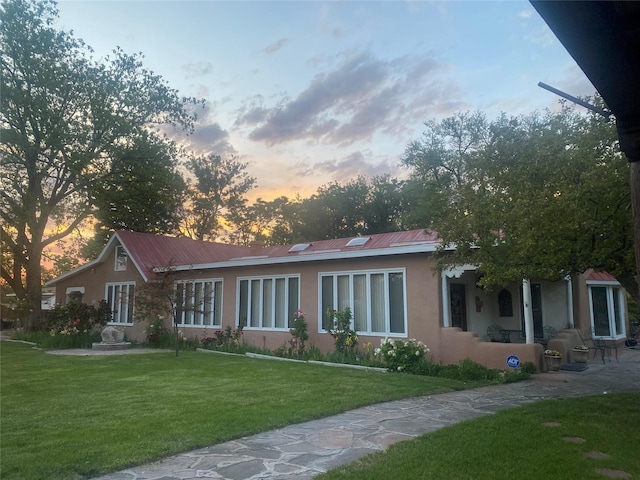 back of house at dusk featuring stucco siding, a yard, and metal roof