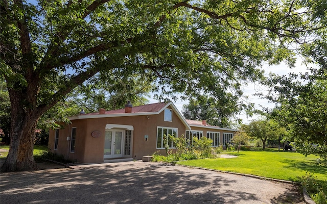 view of front facade featuring a chimney, a front lawn, aphalt driveway, french doors, and stucco siding