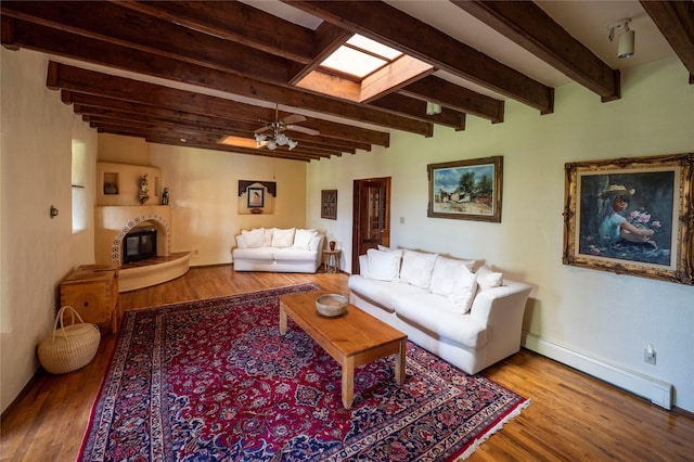 living area with beamed ceiling, a glass covered fireplace, wood finished floors, and a baseboard radiator