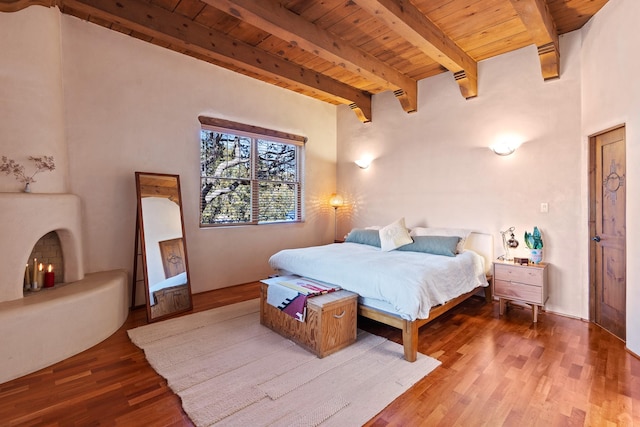 bedroom featuring beamed ceiling, wooden ceiling, wood finished floors, and a lit fireplace