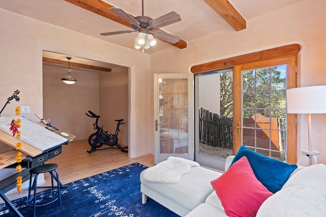 living area featuring a ceiling fan, wood finished floors, and beam ceiling