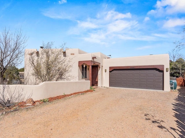 pueblo revival-style home with a garage, driveway, and stucco siding