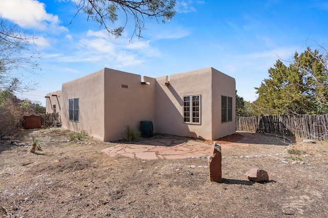 rear view of house with stucco siding and fence