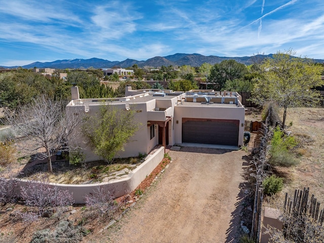 pueblo revival-style home with driveway, a chimney, stucco siding, and a mountain view