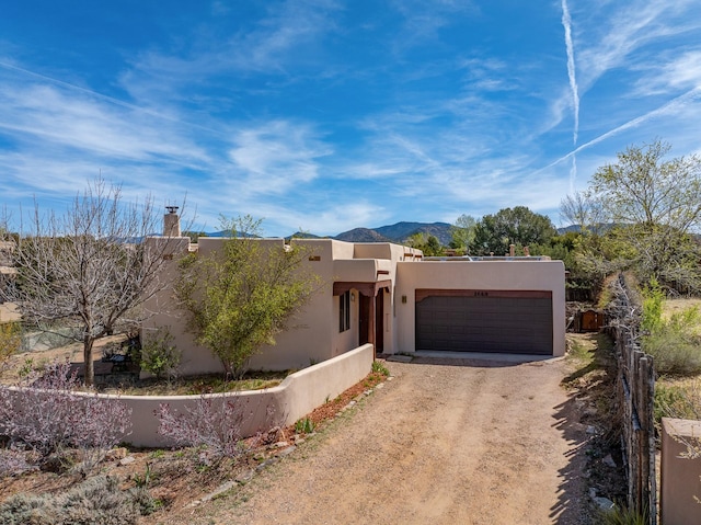 southwest-style home featuring dirt driveway, an attached garage, stucco siding, and a mountain view