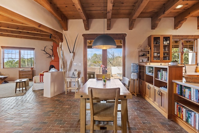 dining space with wooden ceiling, brick floor, and beamed ceiling