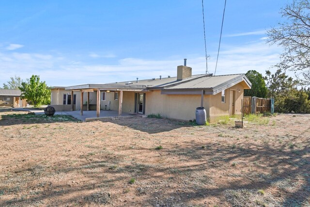 rear view of house featuring a chimney, metal roof, fence, a patio, and stucco siding