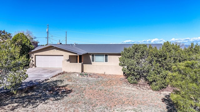 ranch-style house featuring stucco siding, an attached garage, metal roof, and driveway