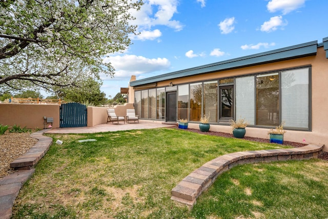 rear view of house with a gate, fence, stucco siding, and a lawn