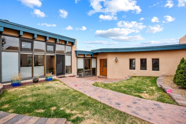 back of house with a lawn and stucco siding