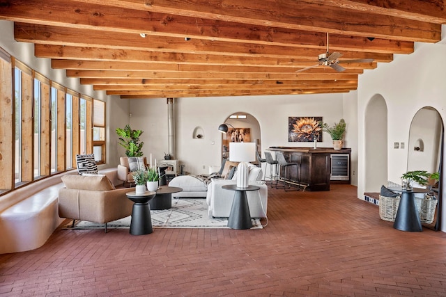 living room featuring brick floor, arched walkways, indoor bar, beam ceiling, and wine cooler
