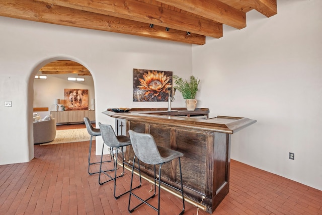 bar featuring beam ceiling, brick floor, a dry bar, and arched walkways