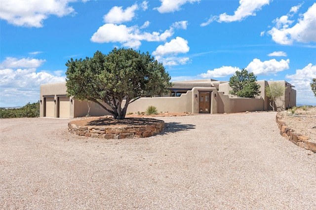 pueblo-style house with stucco siding, an attached garage, a gate, and a fenced front yard