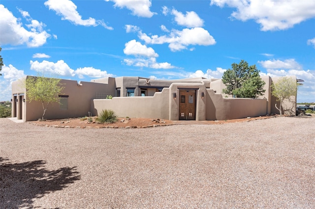 rear view of property featuring stucco siding, gravel driveway, and a fenced front yard