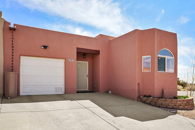 adobe home with an attached garage, driveway, and stucco siding