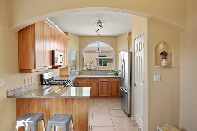 kitchen with light stone counters, a sink, light tile patterned floors, stainless steel appliances, and a peninsula