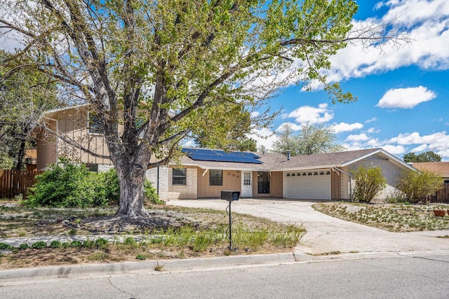 ranch-style home with roof mounted solar panels, an attached garage, fence, and driveway