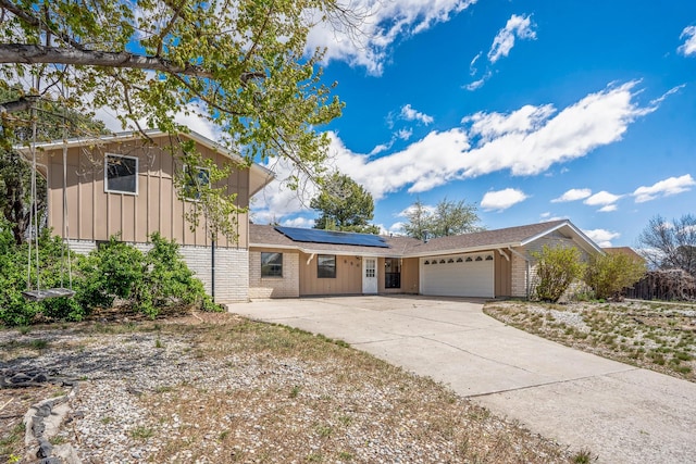 view of front of property with concrete driveway, an attached garage, board and batten siding, solar panels, and brick siding