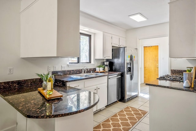 kitchen featuring stainless steel appliances, a peninsula, a sink, light tile patterned flooring, and white cabinetry