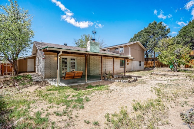 rear view of house featuring a chimney, fence, a patio area, french doors, and brick siding