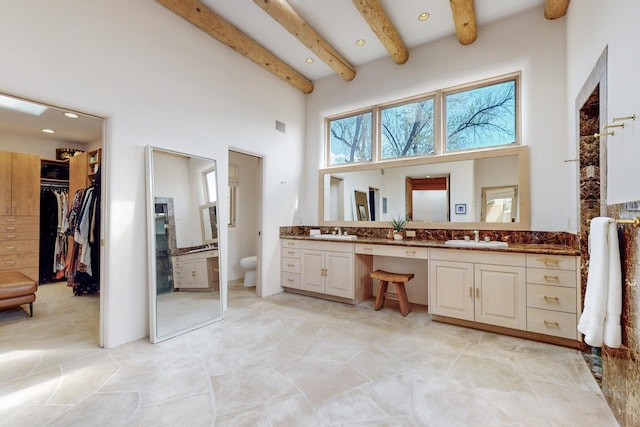 bathroom featuring beamed ceiling, double vanity, a high ceiling, and a sink