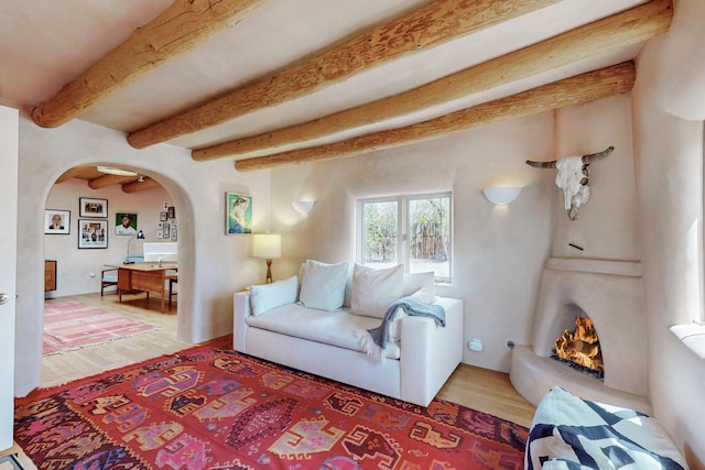 living area featuring arched walkways, wood finished floors, and beamed ceiling