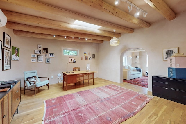 bedroom featuring arched walkways, track lighting, light wood finished floors, and beamed ceiling
