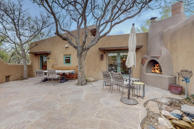 view of patio / terrace with outdoor dining space, french doors, a lit fireplace, and fence