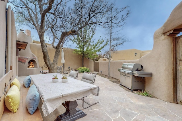 view of patio / terrace with a fenced backyard, a grill, a lit fireplace, and outdoor dining area