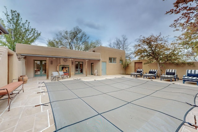 rear view of property with stucco siding, a patio area, a fenced in pool, and french doors