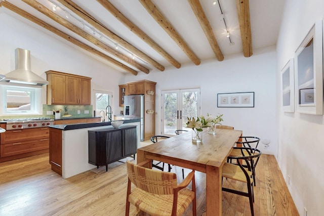 kitchen featuring tasteful backsplash, brown cabinetry, an island with sink, stainless steel appliances, and wall chimney exhaust hood