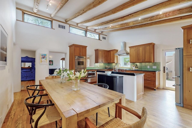 dining area featuring beamed ceiling, light wood-style flooring, visible vents, and a high ceiling