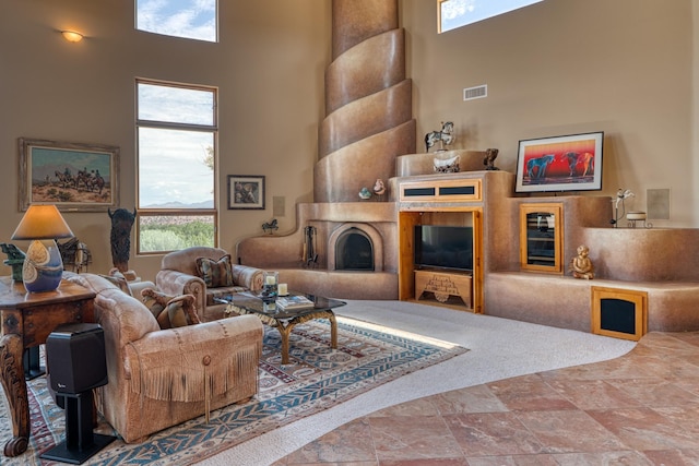 21 Canada Vista Dr, Sandia Park, NM 87047 - living area featuring a fireplace with raised hearth, stone finish floor, a high ceiling, and visible vents