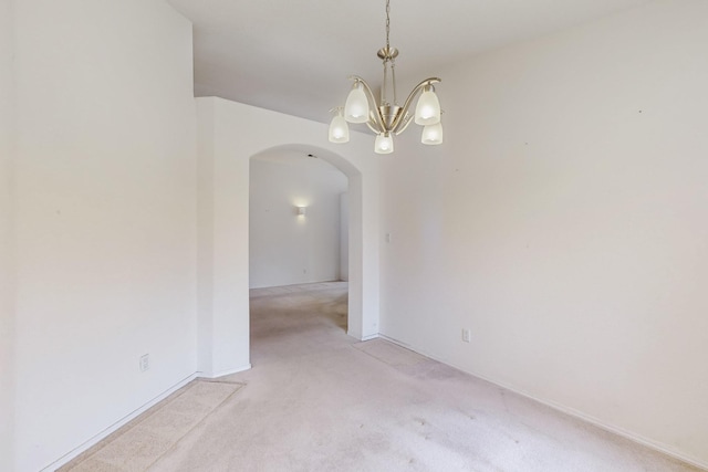 spare room with arched walkways, light colored carpet, and a notable chandelier