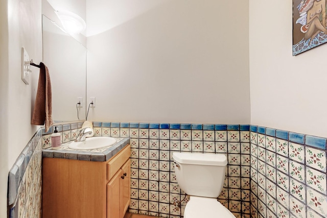 bathroom with tile walls, a wainscoted wall, vanity, and toilet