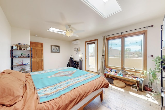 bedroom featuring a skylight, wood finished floors, access to outside, ceiling fan, and a wall mounted AC