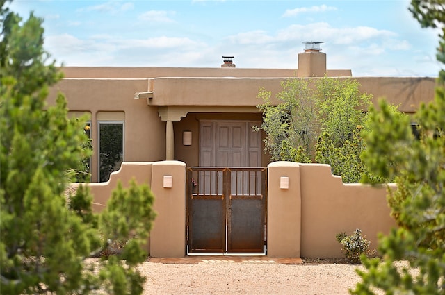 view of exterior entry with a gate, fence, and stucco siding
