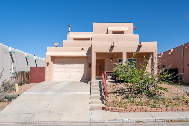 pueblo revival-style home featuring stucco siding, driveway, fence, and a garage