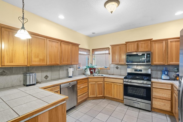 kitchen with a sink, decorative backsplash, appliances with stainless steel finishes, tile countertops, and light tile patterned floors