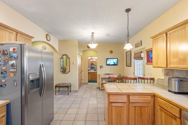 kitchen with tile counters, light tile patterned floors, decorative light fixtures, a peninsula, and stainless steel refrigerator with ice dispenser