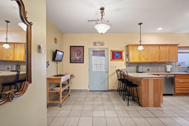 kitchen featuring a peninsula, stainless steel dishwasher, backsplash, light countertops, and a breakfast bar area