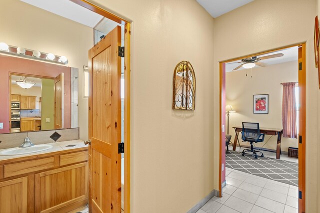 hall featuring light colored carpet, baseboards, light tile patterned flooring, and a sink