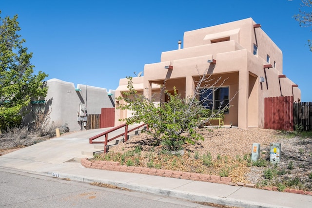 pueblo revival-style home featuring driveway, stucco siding, and fence