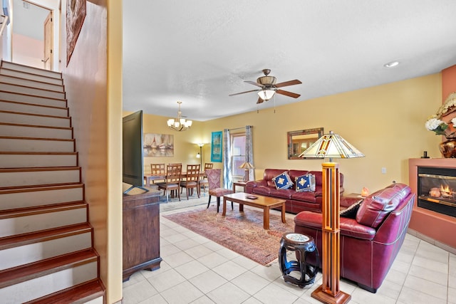 living area featuring ceiling fan with notable chandelier, a glass covered fireplace, light tile patterned floors, and stairway