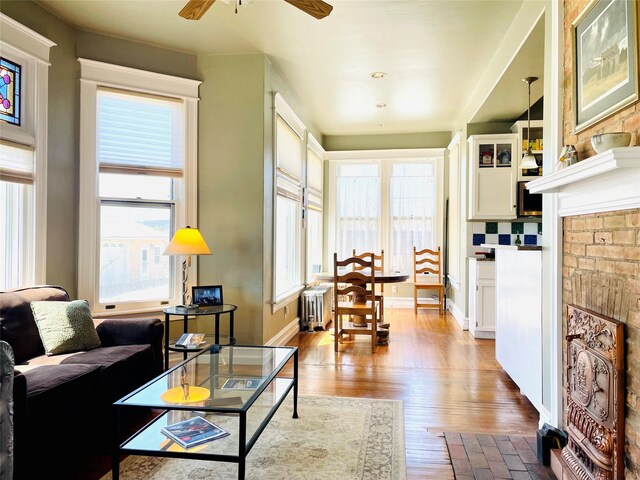 1607 8th St, Las Vegas, NM 87701 - living room featuring radiator, wood finished floors, baseboards, a brick fireplace, and ceiling fan