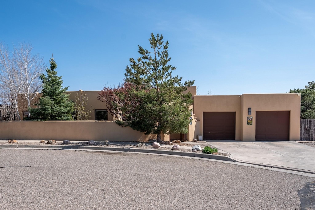southwest-style home featuring stucco siding, an attached garage, driveway, and fence