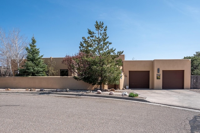 southwest-style home featuring stucco siding, an attached garage, driveway, and fence