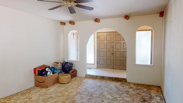 carpeted entrance foyer featuring arched walkways, a ceiling fan, and a wealth of natural light